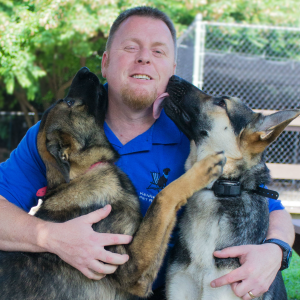 Kevin the Kennelwood Trainer getting licked by two dogs